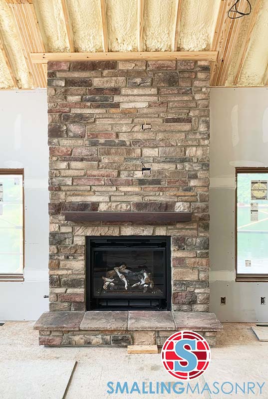 A brown stacked stone fireplace with a dark wood mantlepiece
