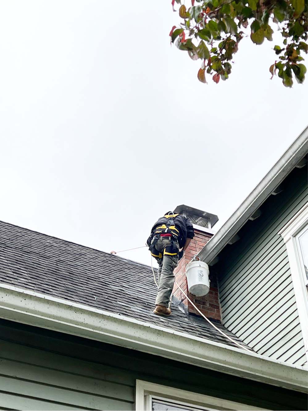 Employee working on a roof wearing protective gear and carrying a white bucket