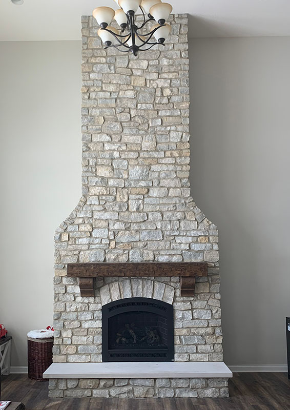 A white gray stone fireplace with a wooden mantelpiece