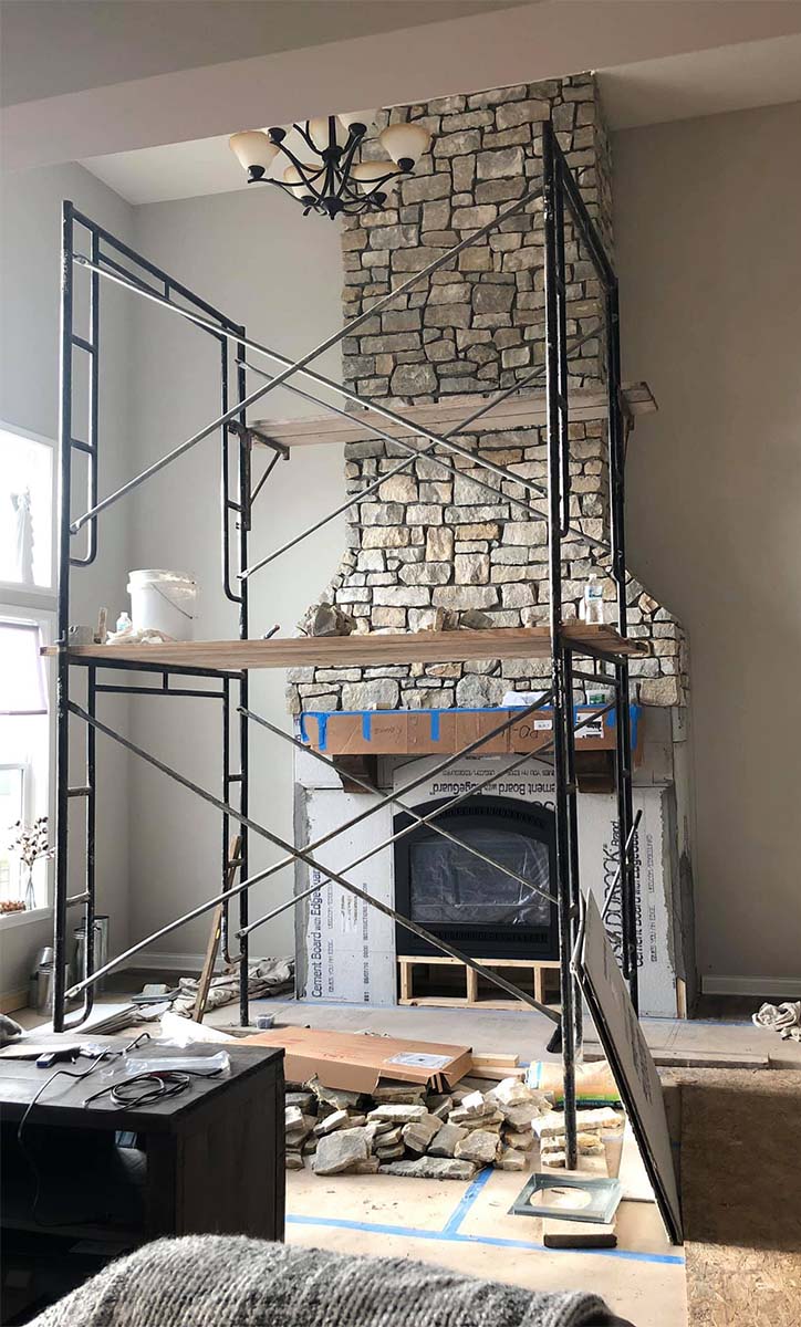A white stone fireplace being built with scaffolding in front.