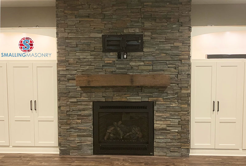 A gray stone fireplace with a dark wood mantlepiece