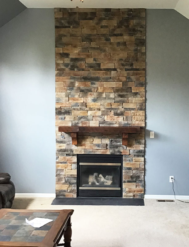 A multicolor stone floor to ceiling surround and fireplace with a wooden mantle piece.