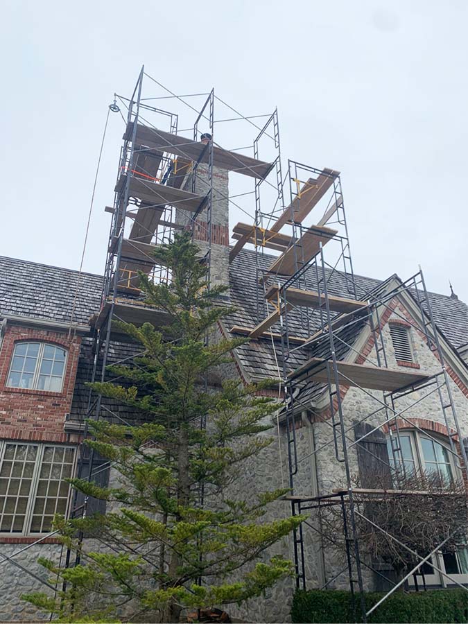 A gray stone and red brick chimney is being rebuilt surrounded by scaffolding.