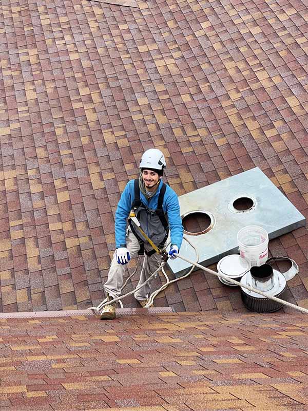 Employee wearing protective equipment on a roof smiling with chimney crown behind him.