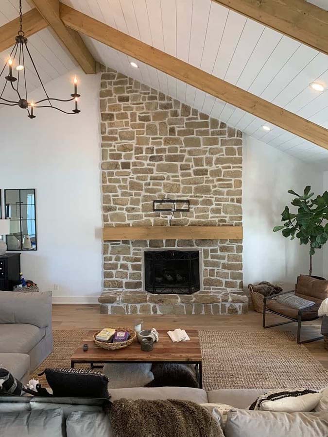 A beige stone fireplace with a white mortar and light wood mantlepiece