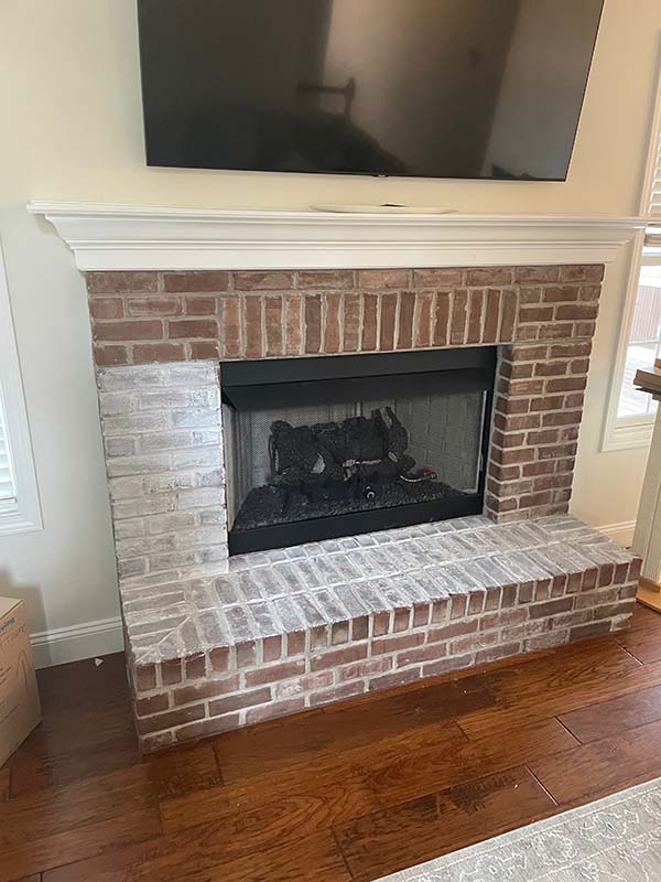 Red brick fireplace that has halfway been painted white before breast wall remodel.