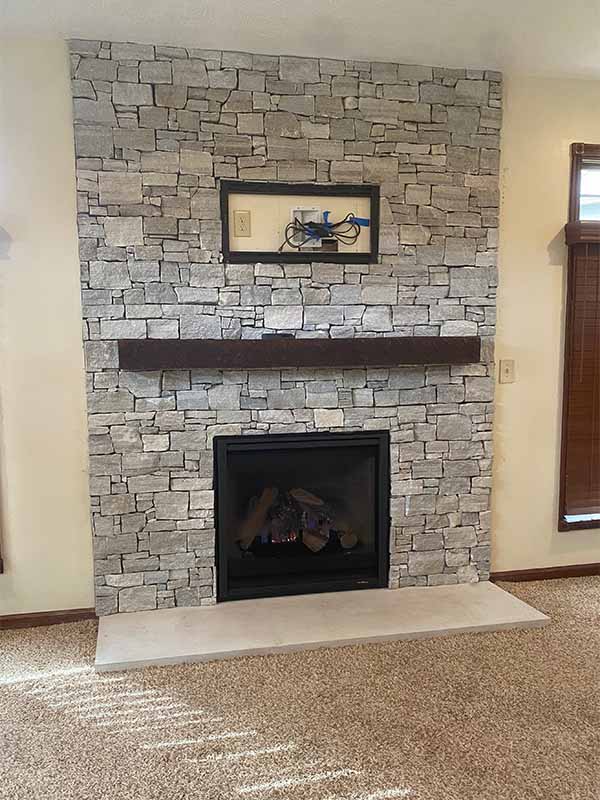 Grey rock fireplace with a dark brown wood mantelpiece after remodel