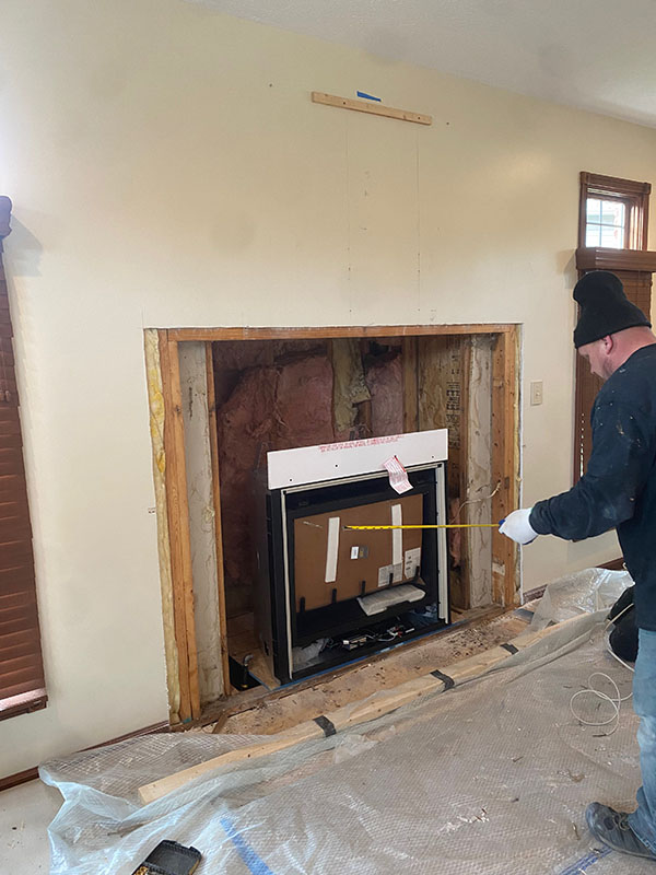 A crew member using a measuring tape in front of a fireplace is being remodeled.