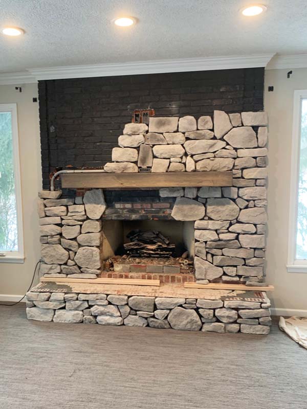 During a fireplace remodel, white and gray stone covering half the fireplace with a light wood beam