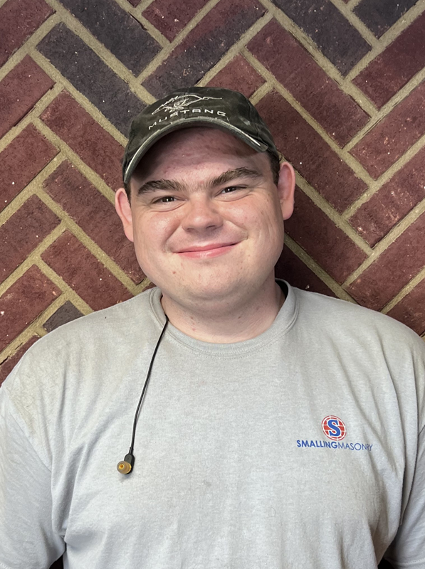 Jacob Ondeka - Consultant - Standing in front of brick wall wearing a black stocking hat and black hoodie with Smalling Logo.  He is wearing black rimmed glasses with a mustache and nice smile.
